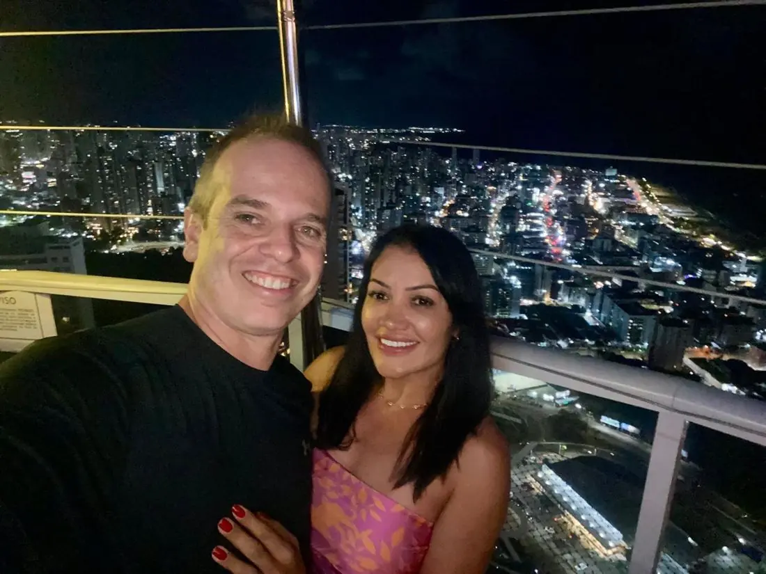 Débora e Marcelo em um terraço com a cidade à noite